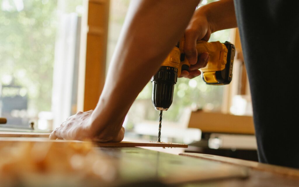 pexels-photo-5974053-5974053 Close-up of a person using a power drill on wood indoors during daytime.